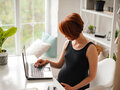 Eine schwangere Frau sitzt vor einem Laptop.